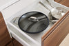 A Misen Carbon Steel Wok with the glass lid on sits in a kitchen drawer with two Misen Stainless Steel pans.